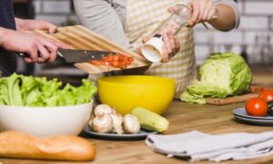 A man and woman are cooking together in a kitchen, preparing ingredients for a meal.