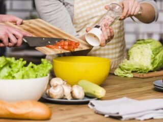 A man and woman are cooking together in a kitchen, preparing ingredients for a meal.