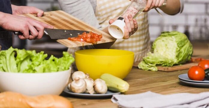A man and woman are cooking together in a kitchen, preparing ingredients for a meal.