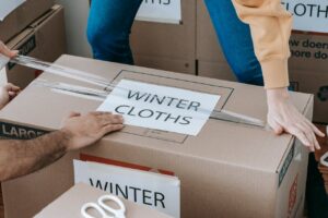 Two people sealing a moving box labeled 'Winter Clothes' as part of smart labeling systems for an organized unpacking process.