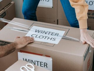 Two people sealing a moving box labeled 'Winter Clothes' as part of smart labeling systems for an organized unpacking process.