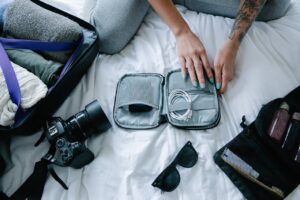 Woman packing cables in a pouch, camera, electronics, luggage on a bed